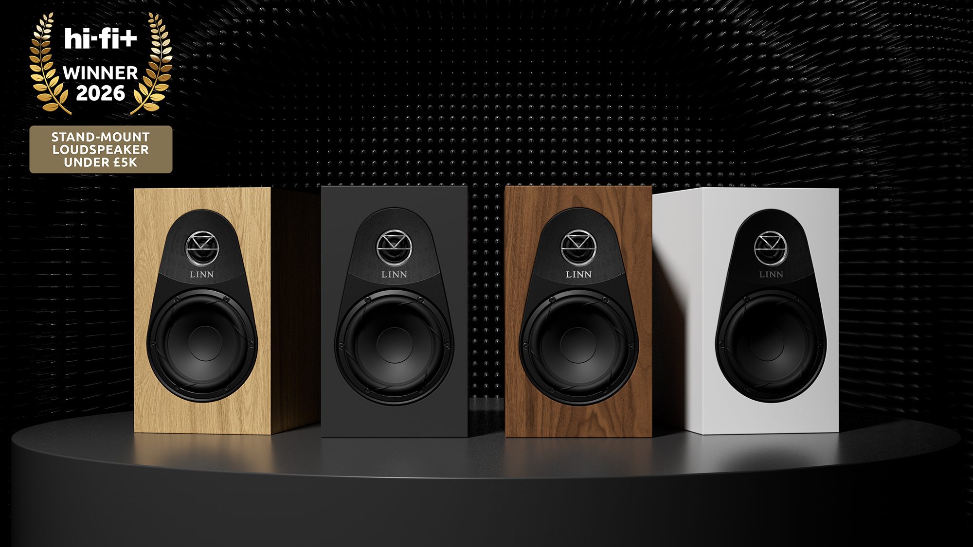 Four Linn 119 stand-mount loudspeakers lined up in Oak, Black, Walnut, and White finishes on a podium, featuring a gold 'Hi-Fi+ Winner 2026' award badge for Best Stand-Mount Loudspeaker Under £5k.