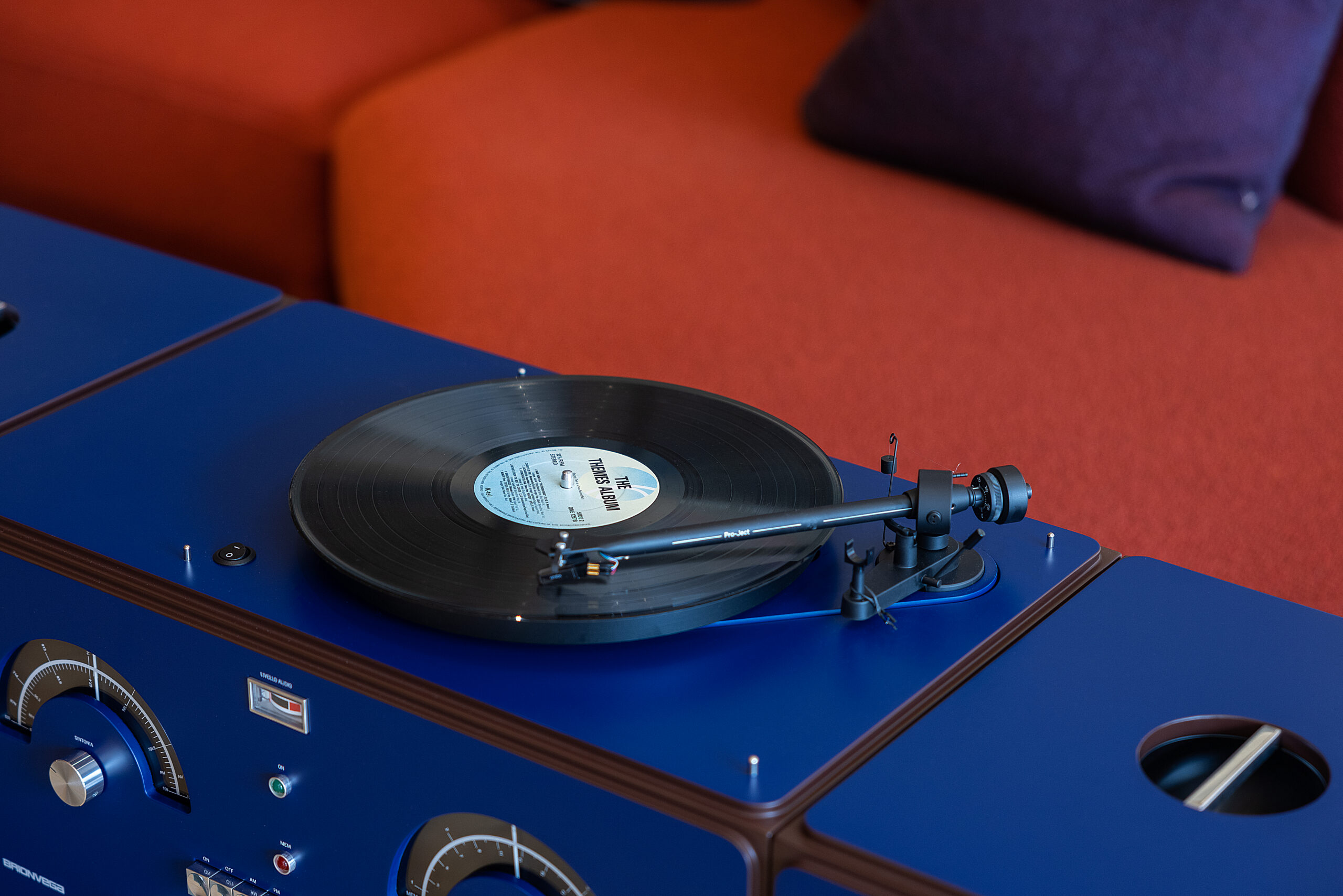 A close-up detail shot of the Brionvega Radiofonografo RR226 in a Cobalt Blue finish, featuring the integrated Pro-Ject tonearm and a spinning vinyl record against a modern interior backdrop.