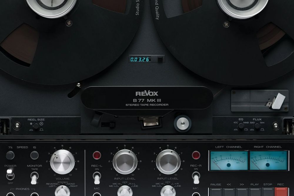 A detailed close-up of the Revox B77 MK III control centre, featuring the modernised high-resolution digital counter and the iconic analog VU meters with integrated peak LEDs for precise level monitoring.